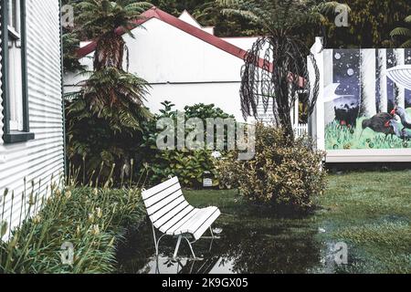 Schöne einsame weiße Holzbank in einsamen ruhigen Park überschwemmt von Regen in einem ruhigen Dorf in der Nähe von Wald, West-Nachbarschaft, Neuseeland Stockfoto