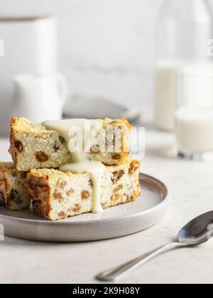 Portion Quark-Auflauf oder Pudding mit Rosinen, die mit Kondensmilch auf weißem Tischhintergrund gegossen wurden Stockfoto