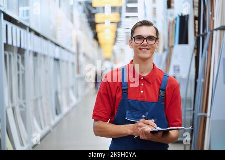 Lächelnder Verkäufer eines Bodenladens, der in einer Halle mit Laminatproben steht. Stockfoto