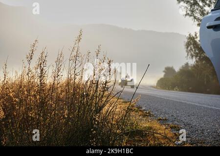 Traktor bei Sonnenaufgang auf der Straße, Blick vom geparkten Auto Stockfoto