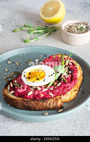 Vollkorn-Toast mit Rübenhummus, Samen, Ei und Mikrogemüse (gekeimt Erbsensprossen) auf hellgrauem Hintergrund. Das Konzept der gesunden Ernährung.. Stockfoto