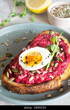 Vollkorn-Toast mit Rübenhummus, Samen, Ei und Mikrogemüse (gekeimt Erbsensprossen) auf hellgrauem Hintergrund. Das Konzept der gesunden Ernährung.. Stockfoto