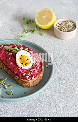 Vollkorn-Toast mit Rübenhummus, Samen, Ei und Mikrogemüse (gekeimt Erbsensprossen) auf hellgrauem Hintergrund. Das Konzept der gesunden Ernährung.. Stockfoto