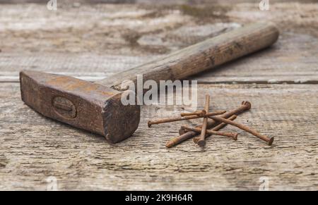 Alter rostiger Hammer und Nägel auf einem unbemalten Holztisch Stockfoto