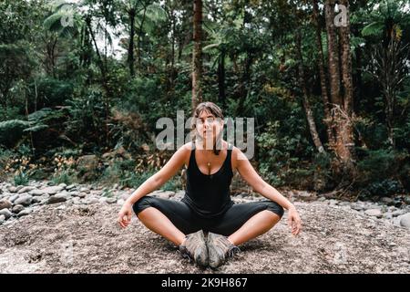 Zerzaust blauäugiges kaukasisches Mädchen mit runden Ohrringen und einer Halskette am Hals, das die Kamera mit ausgestreckten Armen auf ihr sitzend ansah Stockfoto