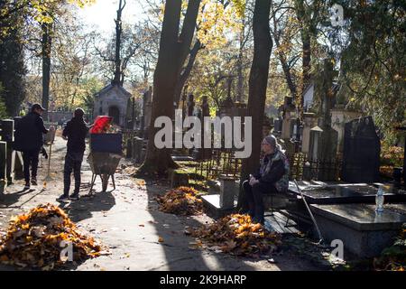 Zwei Männer fegen Blätter auf dem historischen Powazki Friedhof. Der Allerheiligste Tag, der am 1.. November stattfindet, ist ein Feiertag in Polen und einer der wichtigsten katholischen Feiertage im Laufe des Jahres. Diejenigen, die ihre Angehörigen verloren haben, gehen auf die Friedhofs, um den Toten ihre Achtung zu erweisen. Sie brennen Kerzen auf den Gräbern und bringen Blumen. Es wird manchmal auch als der Tag der Erinnerung an die, die gegangen sind, bezeichnet. Stockfoto