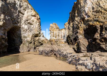 Felsformationen und Höhlen am Perranporth Beach in Cornwall, mit einem blauen Himmel über dem Strand Stockfoto