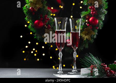 Zwei gefüllte Sektgläser vor dem Hintergrund eines Weihnachtskranzes. Babbo Natale, Uvlin Uvgun, joulupukki, Nikolaus, Weihnachtsmann Weihnachten Stockfoto