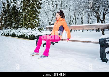 Wintertraining im Freien. Winterfitness, Training bei kaltem Wetter. Sportlerin macht Dehnübungen und bereitet sich auf das Laufen in der Natur vor Stockfoto