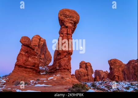 Ein atemberaubendes Landschaftsfoto zeigt eine Ansammlung von hoch aufragenden roten Felsformationen vor einem leuchtend blauen Himmel in der Dämmerung und einem aufgehenden Mond. Stockfoto