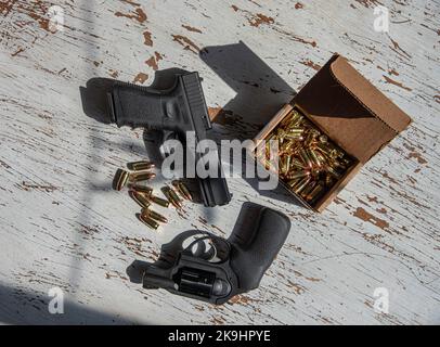 Eine Glock-Pistole von 9mm und ein Ruger-Revolver von 9mm mit einer Schachtel mit 9mm Patronen auf einem Tisch. Stockfoto