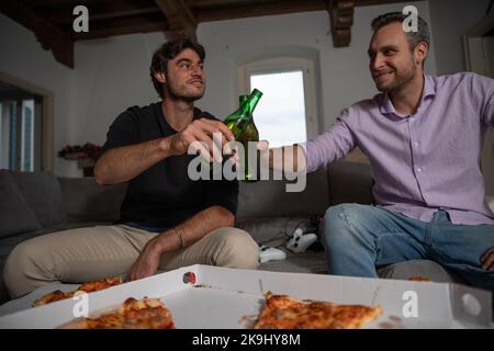Zwei Freunde stoßen mit zwei Bieren in der Pause von Videospiel Pizza essen. Stockfoto