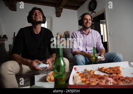 Freunde, die Spaß beim Spielen bei Videospielen haben, während sie Pizza essen und Bier trinken. Stockfoto