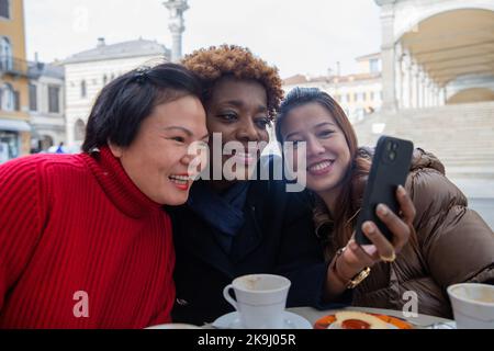 Lächelnde Freunde, die Spaß haben, etwas auf dem Handy zu teilen. Diversity-Konzept. Stockfoto