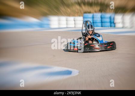 Zoom-Effekt eines Teenagers, der einen Kart am Ausgang einer Kurve eines Kart-Rundgangs fährt, Gesicht der Geschwindigkeit und Konzentration, während er einen Kart fährt, defo Stockfoto