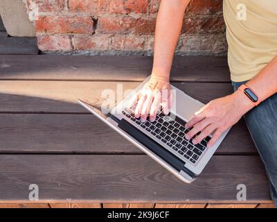 Draufsicht auf die Hände des Mannes auf der Computertastatur. Freiberufler arbeitet im Freien mit einem Laptop. Moderner Lifestyle. Open-Air-Arbeitsplatz. Stockfoto