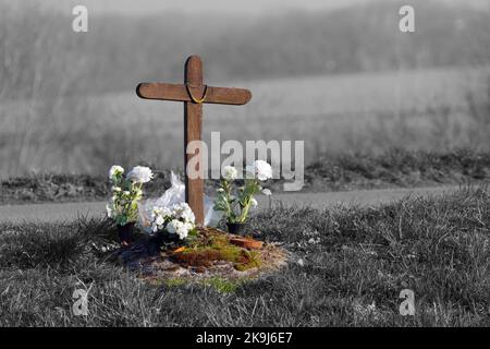 Einfaches Holz Kreuz und Blume auf einem Friedhof Grab in der Natur neben der Straße Stockfoto