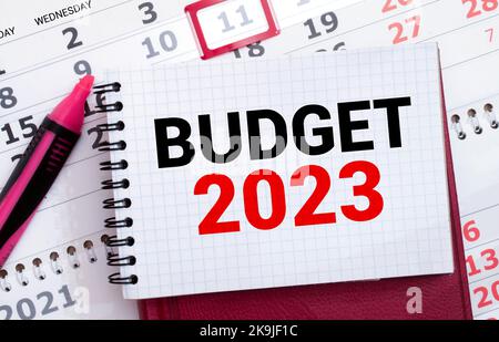 Notizblock mit Text BUDGET 2023, Brille, Büroklammern, weißem Taschenrechner und Stift auf Desktop, Draufsicht Stockfoto