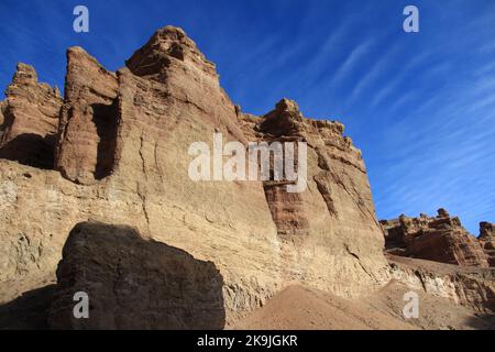 Hohe steile sandig-lehmige Felsen der Charyn-Schlucht gegen den Himmel mit welligen Wolken bei sonnigem Wetter Stockfoto