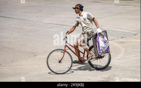 SAMUT PRAKAN, THAILAND, Okt 04 2022, Ein Mann fährt ein Fahrrad und hält eine Last in einer Hand Stockfoto