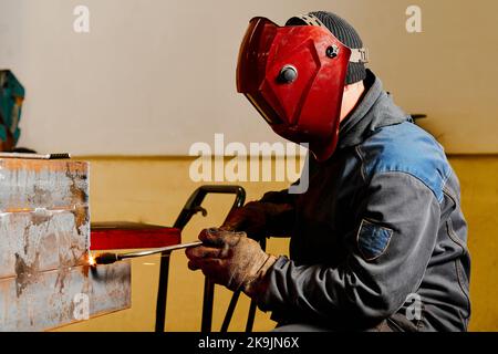 Mitarbeiter mit Maske schneidet Balken mit Heißgasabschneider im Werk Stockfoto