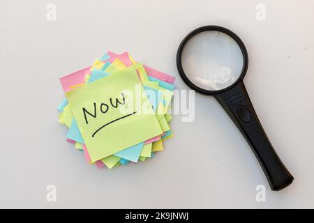 Handgeschriebenes Wort JETZT auf einem klebrigen Papierzettel auf einem weißen isolierten Hintergrund Stockfoto