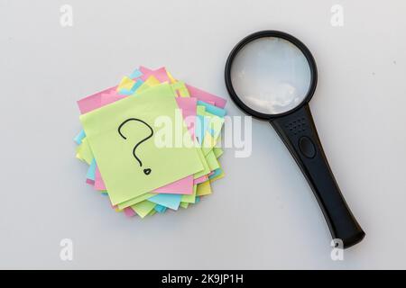 Das Fragezeichen Zeichen Hand auf einem Haftnotiz entlang einem Suchwerkzeug der Lupe geschrieben Stockfoto