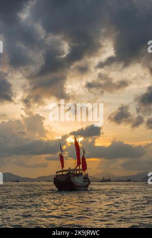 Die „Aqua Luna“, eine nachgebaute chinesische Dschunke, segelt nach Westen in die untergehende Sonne, während sie Touristen auf einer Vergnügungskreuzfahrt durch den Victoria Harbour, Hongkong, transportiert Stockfoto