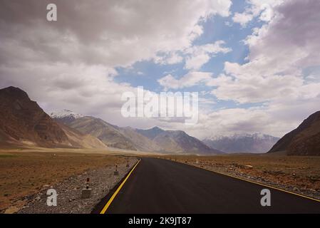 Eine Asphaltstraße erstreckt sich über eine weite, offene Ebene in der Höhenregion von Ladakh Zanskar im nordindischen Himalaya Stockfoto