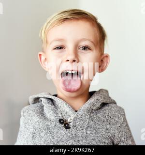 Sagen Sie aaaaah. Porträt eines fröhlichen kleinen Jungen, der tagsüber zu Hause seine Zunge herausstreckt. Stockfoto