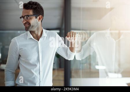 Moderner Mann in einem modernen Büro. Ein hübscher junger Geschäftsmann, der sich in seinem modernen Büro an einer Glaswand lehnt. Stockfoto