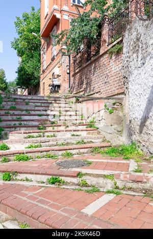 Gehweg mit roten Ziegeltreppen führt zu alten traditionellen Gebäude und Bäumen, an sonnigen Tagen, Balat-Viertel, Istanbul, Türkei Stockfoto