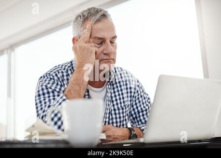 Stress betrifft uns alle. Ein reifer Mann, der gestresst aussieht, während er zu Hause an einem Laptop arbeitet. Stockfoto