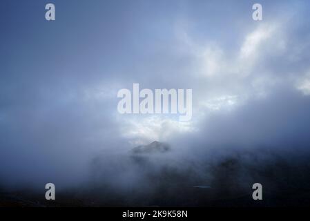 Nahaufnahme von kaum sichtbaren Bergen, umgeben von Nebel und Wolken Stockfoto