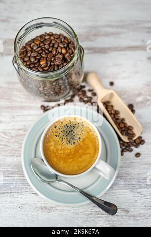 Frisch gebrühter Kaffeebecher und Glas mit gerösteten Kaffeebohnen auf einem Vintage-Tisch. Stockfoto