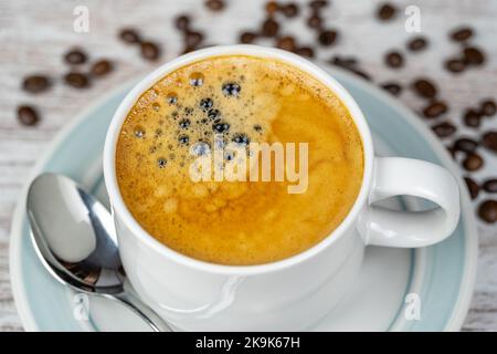 Weiße Porzellantasse mit einem frisch gebrühten Espresso und Kaffeebohnen auf dem Tisch. Stockfoto