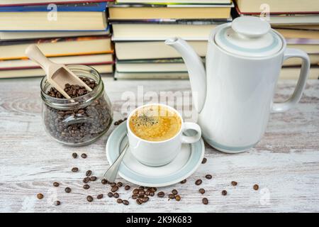 Kaffeebecher mit Kaffeemaschine aus Porzellan und Glas mit Kaffeebohnen mit einem Hintergrund von Büchern in der Bibliothek Stockfoto