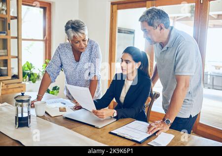 Ihre Investitionen sehen ziemlich profitabel aus. Ein reifes Paar erhält Beratung von ihrem Finanzberater zu Hause. Stockfoto