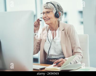 Professionalität und Fachwissen sind in jedem Anruf enthalten. Eine glückliche ältere Frau, die in einem Callcenter arbeitet. Stockfoto