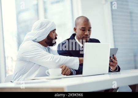 Zwei Geschäftsleute, die ein digitales Tablet und einen Laptop benutzen, während sie in einem modernen Büro eine Diskussion führen. Stockfoto