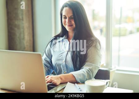 Wir melden uns in der Welt an. Eine junge Frau, die einen Laptop in einem Café benutzt. Stockfoto