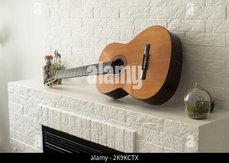 Minimalistisches Innenraumkonzept. Akustikgitarre auf grauem Textil-Sofa in geräumigen Zimmer im Loft-Stil Wohnung mit Holz strukturiert laminiert Stockfoto