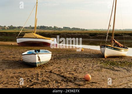 Boote ruhen in Blakeney, Norfolk, an einem sonnigen Abend bei Ebbe, neben dem Fluss. Die Boote heißen Silver Cub und Trinity Stockfoto