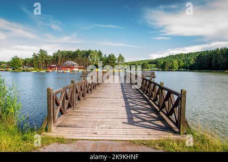 Ein wunderschöner hölzerner Pier über der Lagune. Die goldene Stunde an der Lagune, umgeben von Pinienwäldern. Krasnobród, Polen Stockfoto