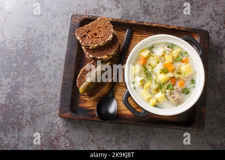 Ogorkowa Zupa cremige polnische Dill Pickle-Suppe mit Wurzelgemüse in der Nähe auf dem Topf auf dem Holztablett. Horizontale Draufsicht von oben Stockfoto