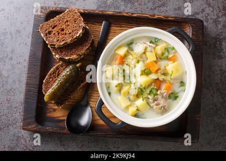 Ogorkowa Polnische Sour Pickle Suppe Nahaufnahme auf dem Topf auf dem Holztablett. Horizontale Draufsicht von oben Stockfoto