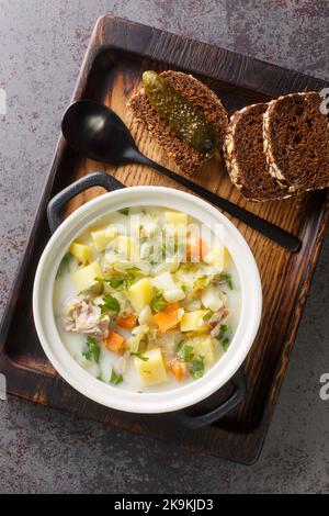 Cremige Pickle-Suppe Zupa Ogorkowa Nahaufnahme auf dem Topf auf dem Holztablett. Vertikale Draufsicht von oben Stockfoto