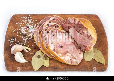 Rumänisches traditionelles Gericht namens Toba oder Piftie, hergestellt aus Schweineorganen in natürlicher Mammutmammbran, Scheiben auf einem Holzbrett mit Knoblauch, Lorbeerblättern und Pfeffer Stockfoto