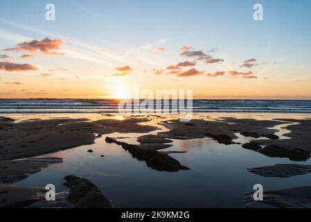 Schönes Landschaftsbild im Sommer bei Sonnenuntergang von Widemouth Bay in Devon England mit goldenem Stundenlicht am Strand Stockfoto