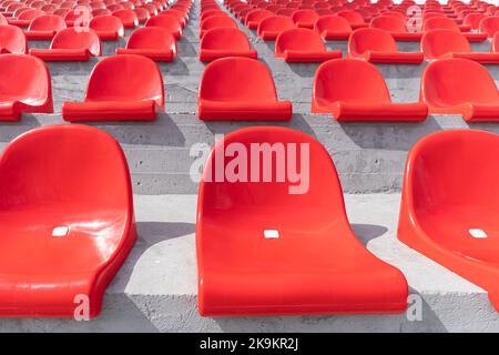 Reihen von roten Stadionsitzen aus Kunststoff. Leere Plätze auf dem Podium ohne Menschen. Stockfoto